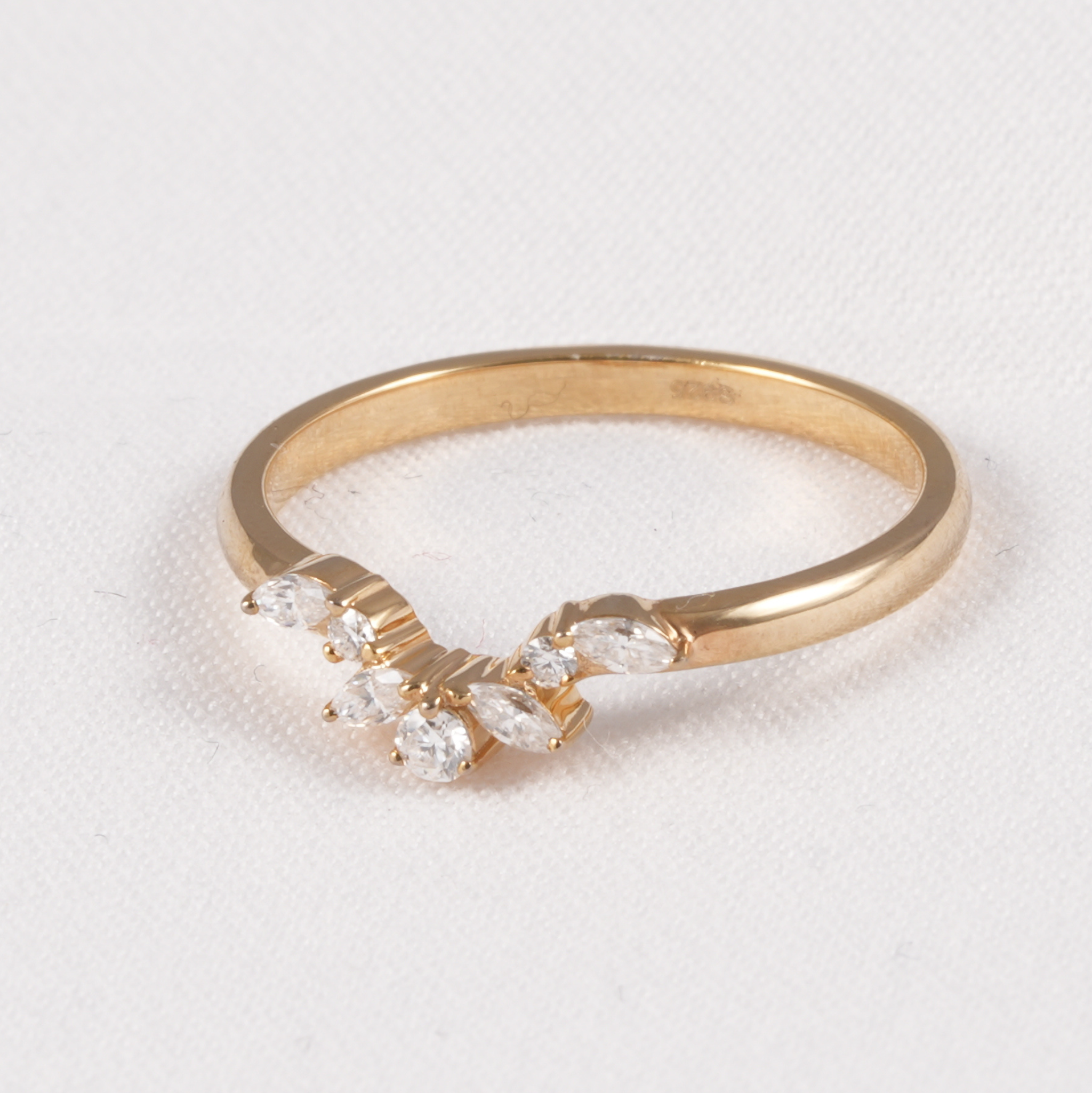 A yellow gold ring featuring a curved row of marquise-cut clear gemstones on a textured white background.