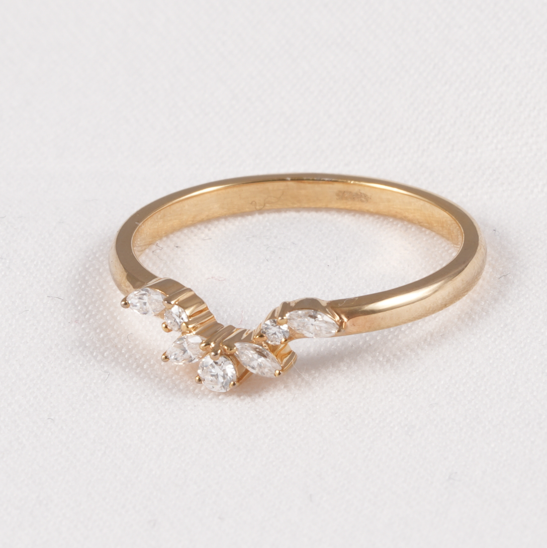 A yellow gold ring featuring a curved row of marquise-cut clear gemstones on a textured white background.