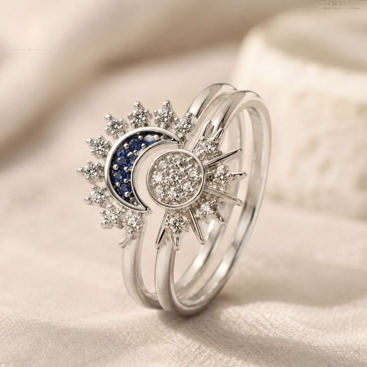 A silver-toned double ring set featuring a celestial sun and moon design. The left ring has a crescent moon paved with small blue stones, while the right ring features a sun face paved with clear cubic zirconia.
