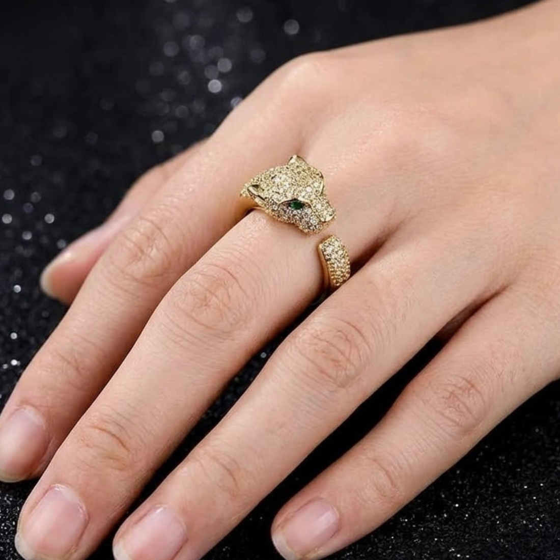 A gold ring featuring a detailed leopard head on one band and a smaller matching ring on the other band, worn on a hand against a dark glittery background.
