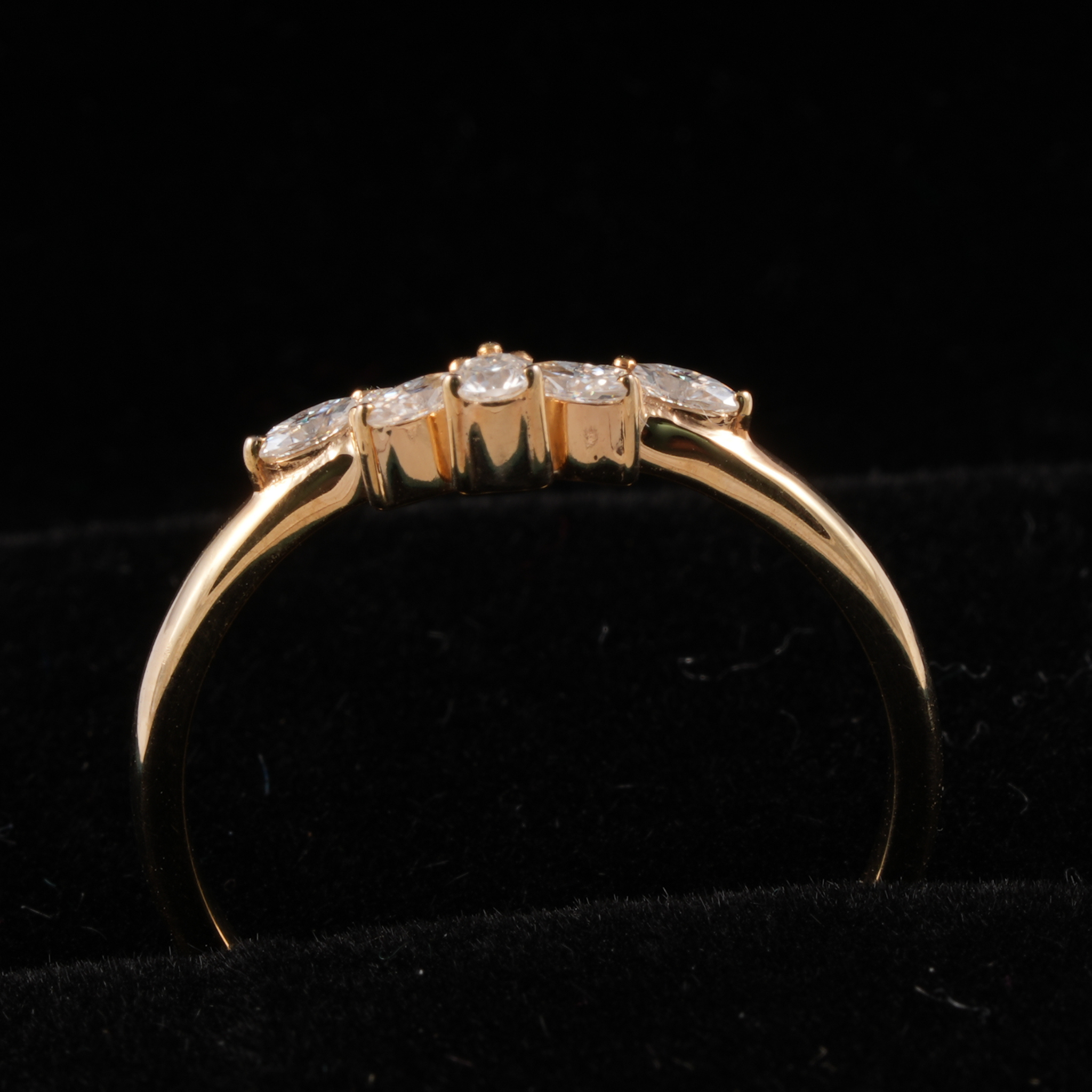 A yellow gold ring with a curved band and a row of four clear round-cut gemstones, displayed on a black velvet surface.