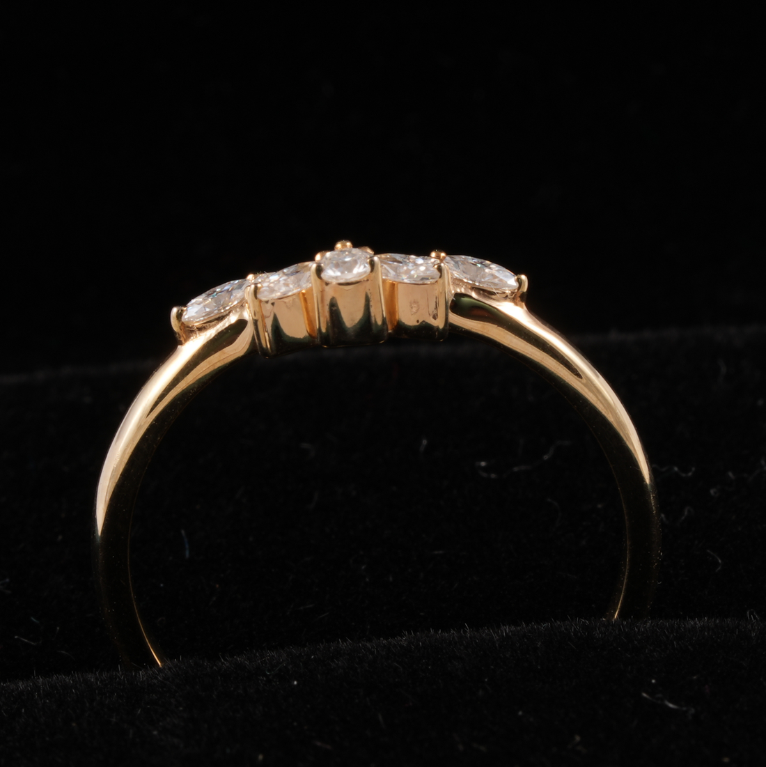 A yellow gold ring with a curved band and a row of four clear round-cut gemstones, displayed on a black velvet surface.