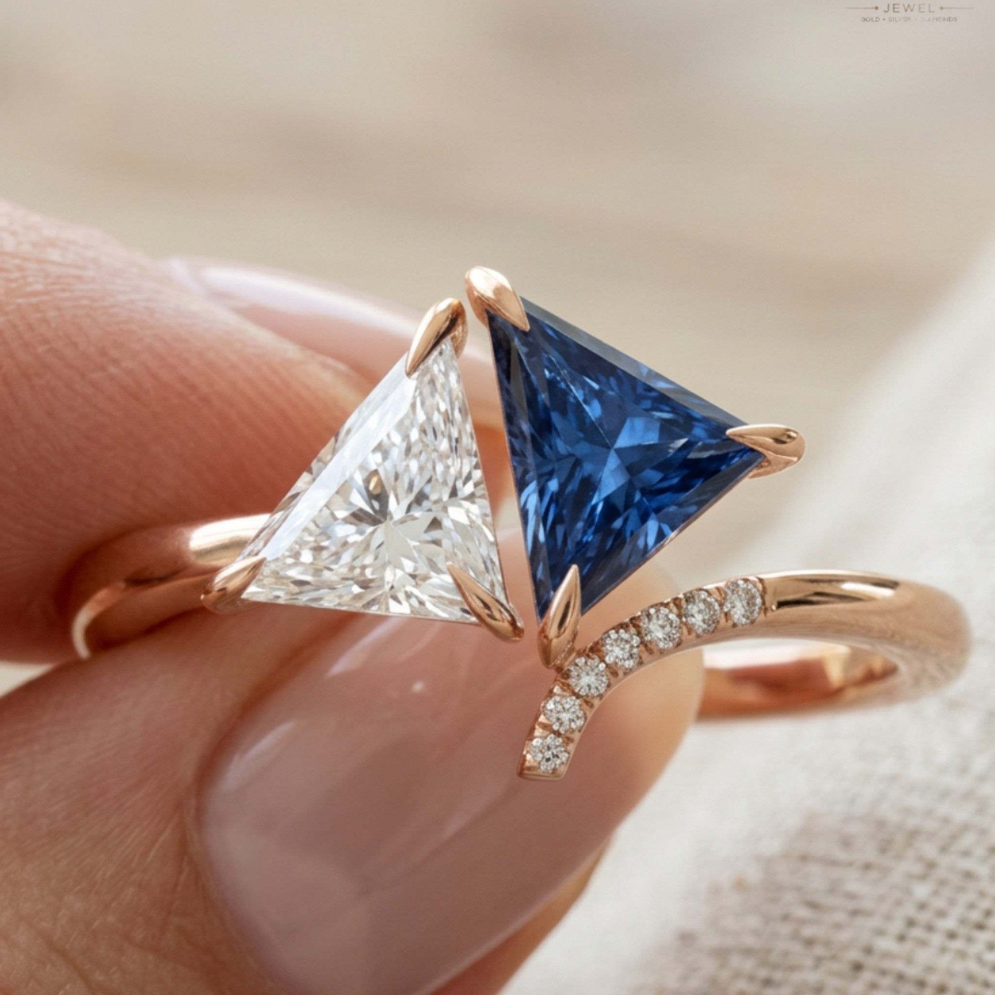 A close-up of a hand wearing a rose gold ring with a split triangular gemstone design, featuring one clear princess-cut diamond and one deep blue princess-cut sapphire, with a curved pavé band.