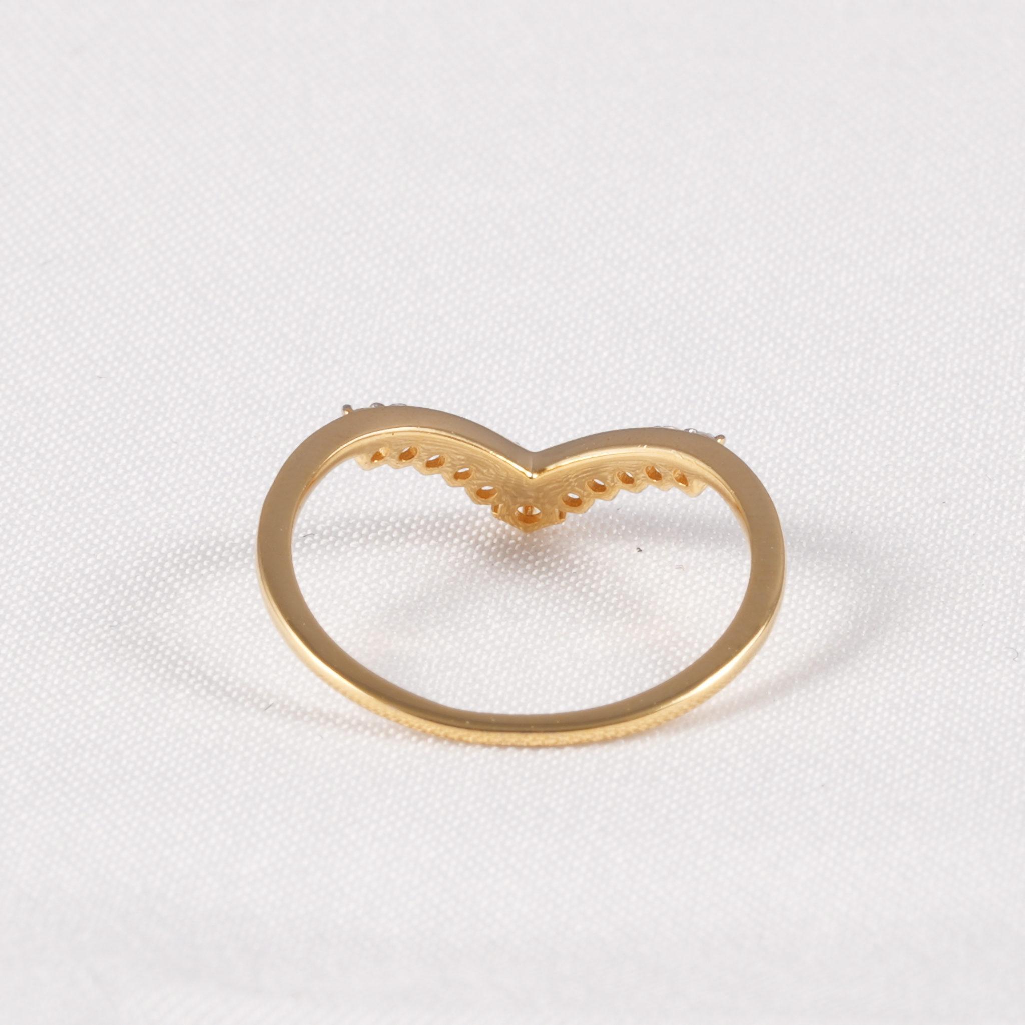 A gold heart-shaped ring setting or decorative piece on a textured white fabric background.