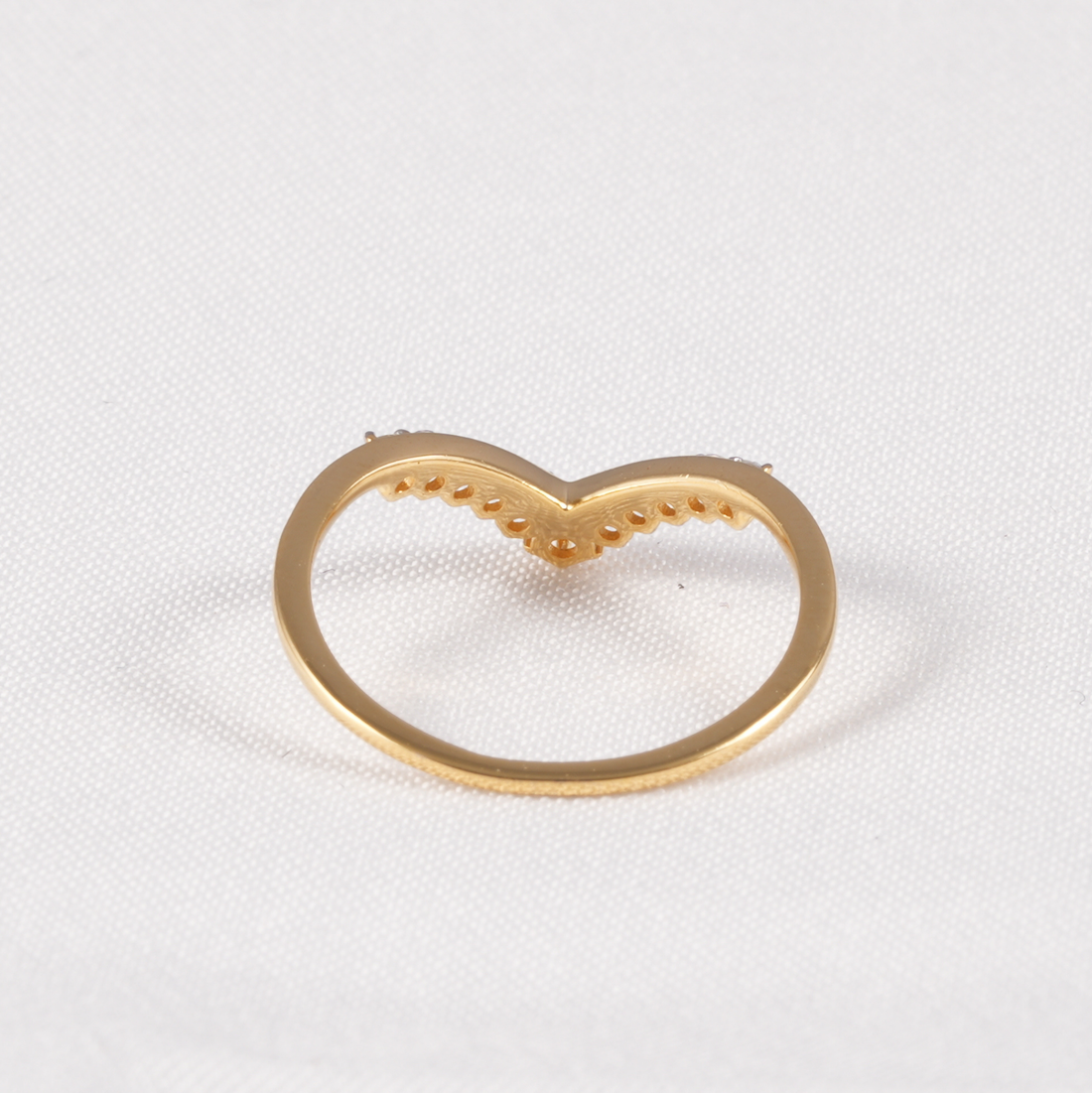 A gold heart-shaped ring setting or decorative piece on a textured white fabric background.