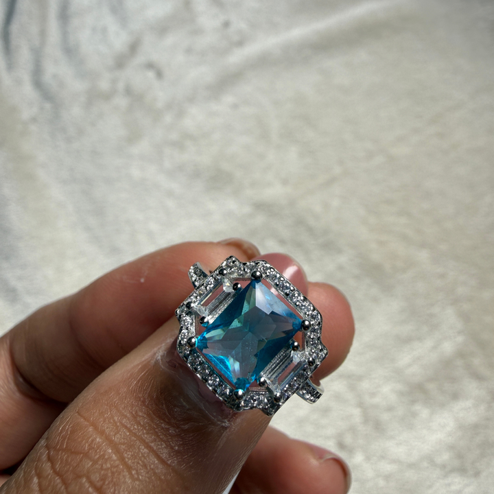 Blue emerald-cut gemstone and lab-grown diamond halo ring by Kiashaa Jewellery.