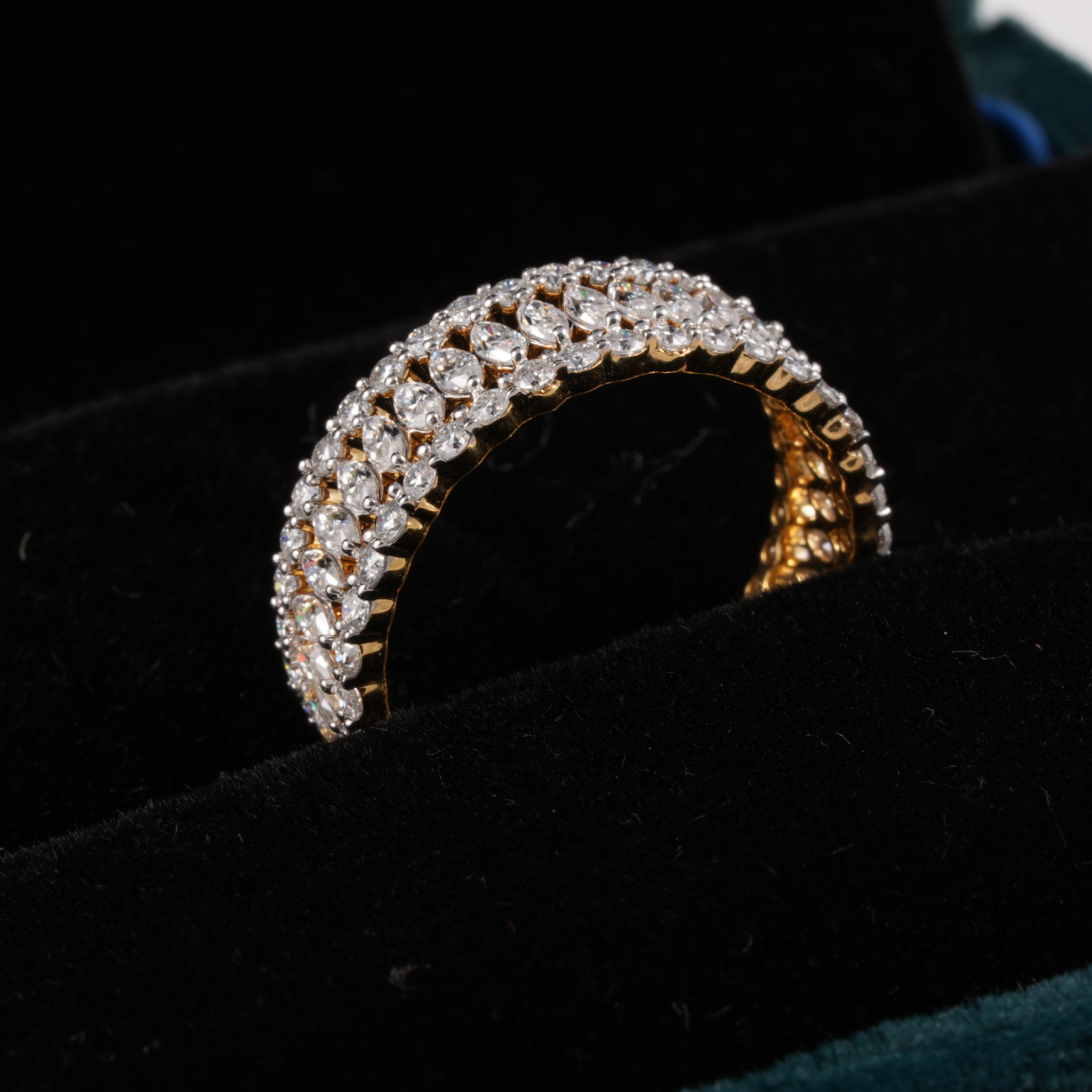 A gold ring with multiple rows of clear round-cut gemstones, displayed on a black velvet jewelry box.