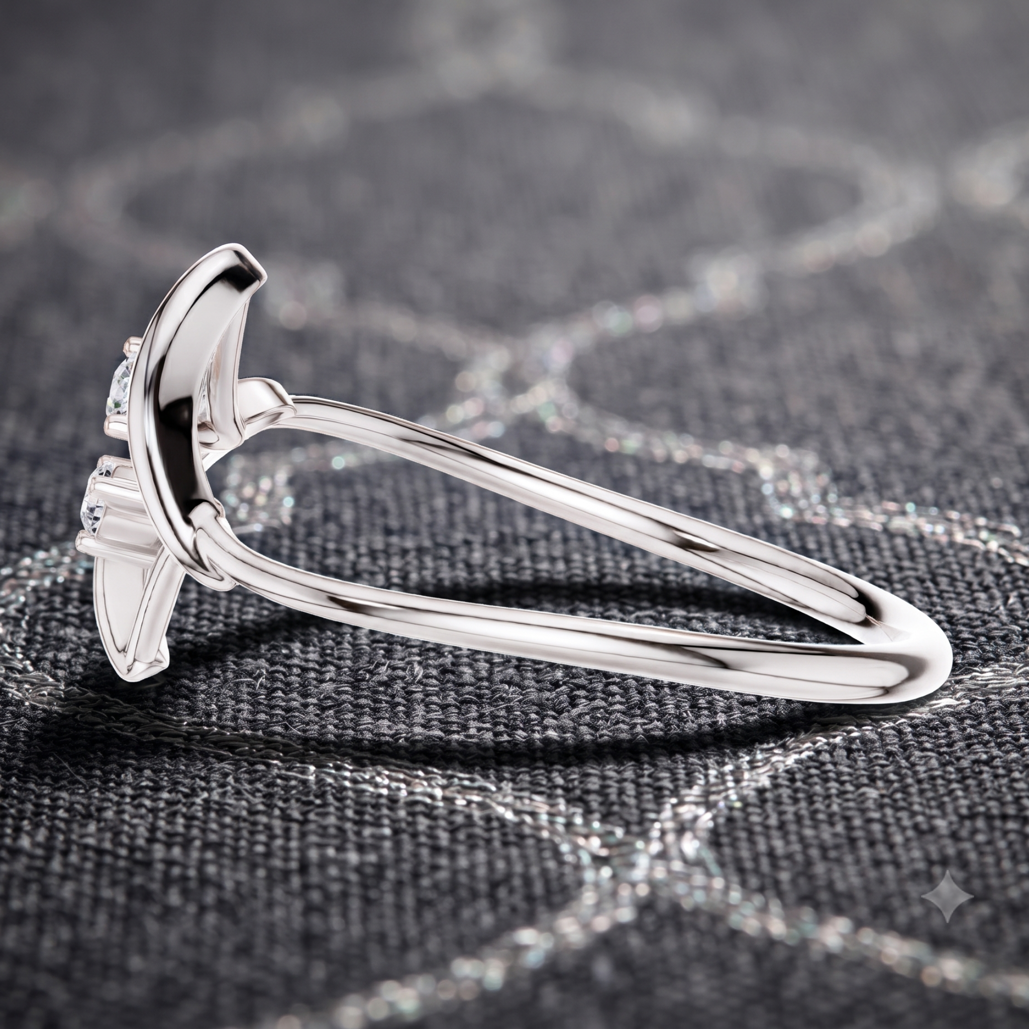 A polished silver ring with a curved, wing-like top setting and small clear stones, photographed close up on a dark textured fabric background.