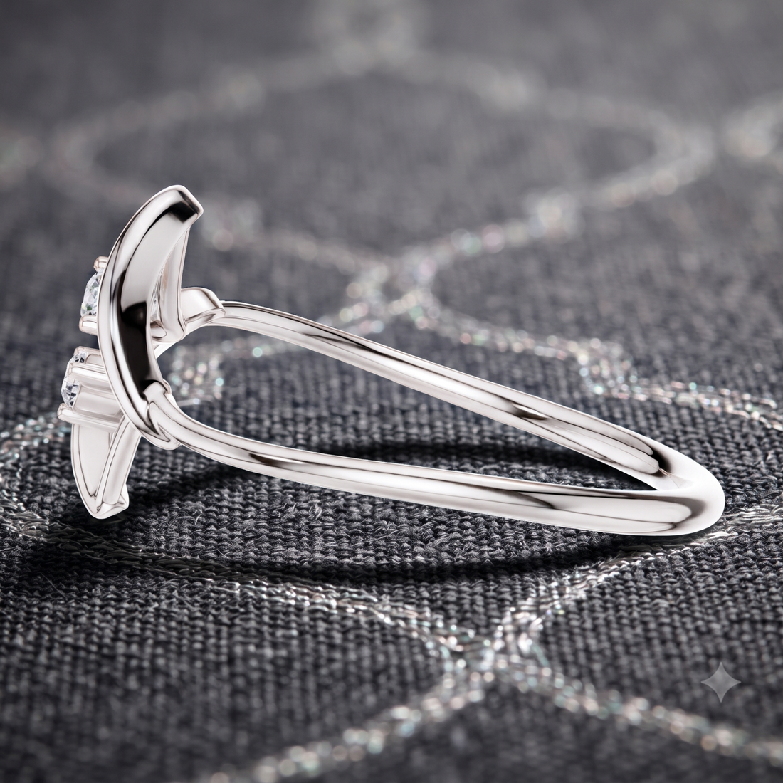 A polished silver ring with a curved, wing-like top setting and small clear stones, photographed close up on a dark textured fabric background.