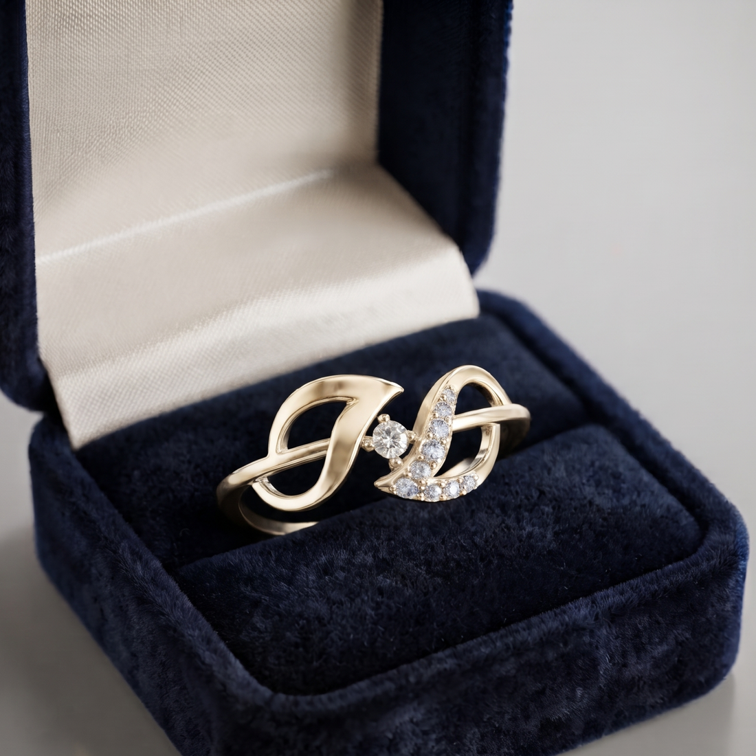 A gold ring with a double swan motif and a small central clear gemstone, displayed in an open dark blue velvet ring box with a cream satin lining.