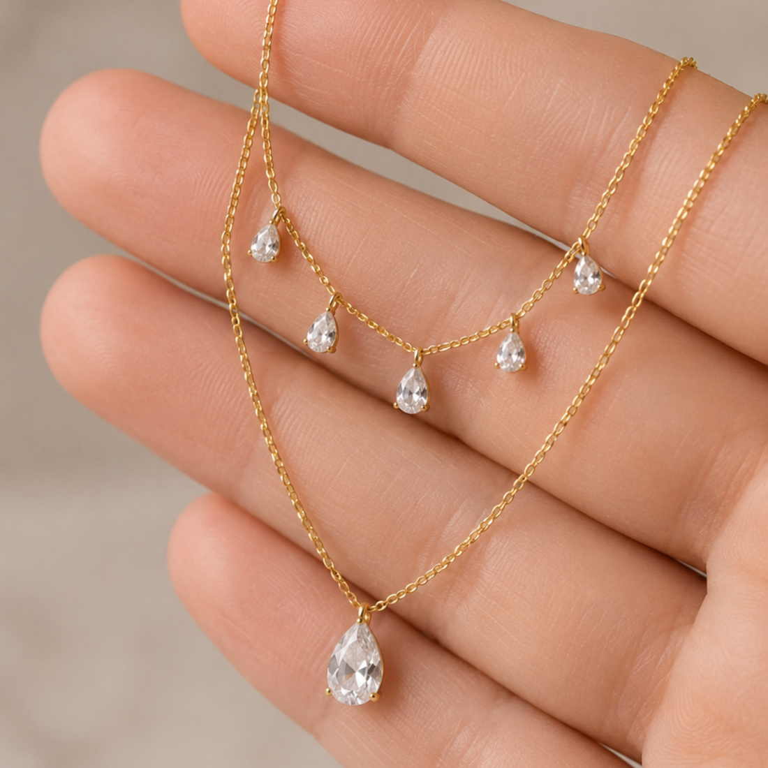 A delicate gold necklace with five dangling teardrop-shaped clear gemstones, draped across a person's hand to show scale and detail.