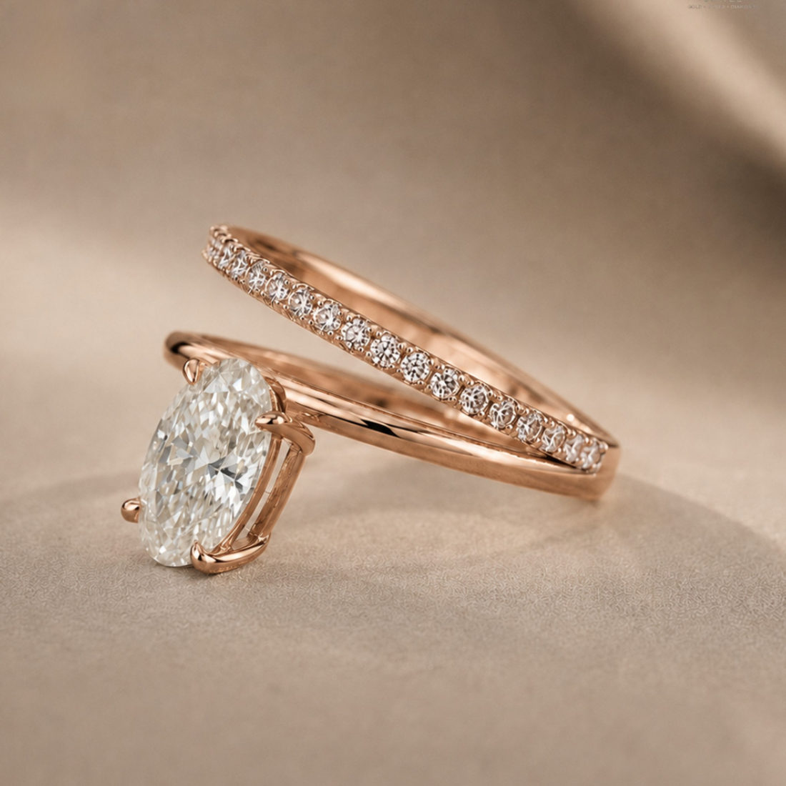 Rose gold engagement ring with a large oval-cut diamond and a matching pavé band ring, displayed on a soft beige fabric background.