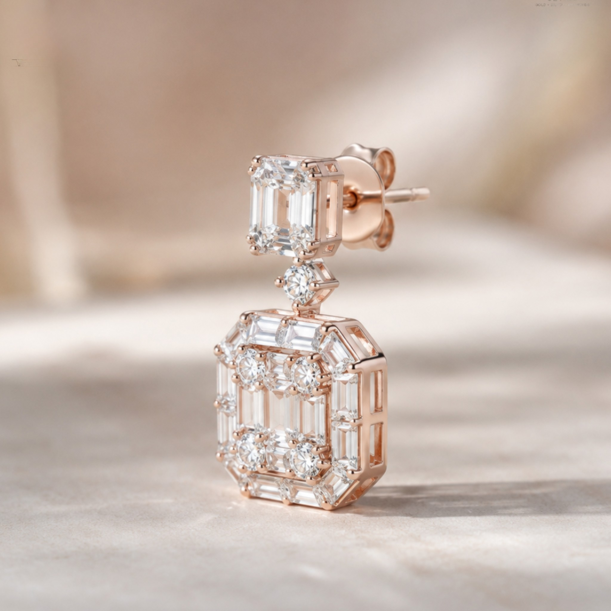 A rose gold drop earring featuring a smaller top section with a clear baguette gemstone and a larger bottom section with multiple clear baguette and round-cut stones, set in rose gold on a soft beige background.