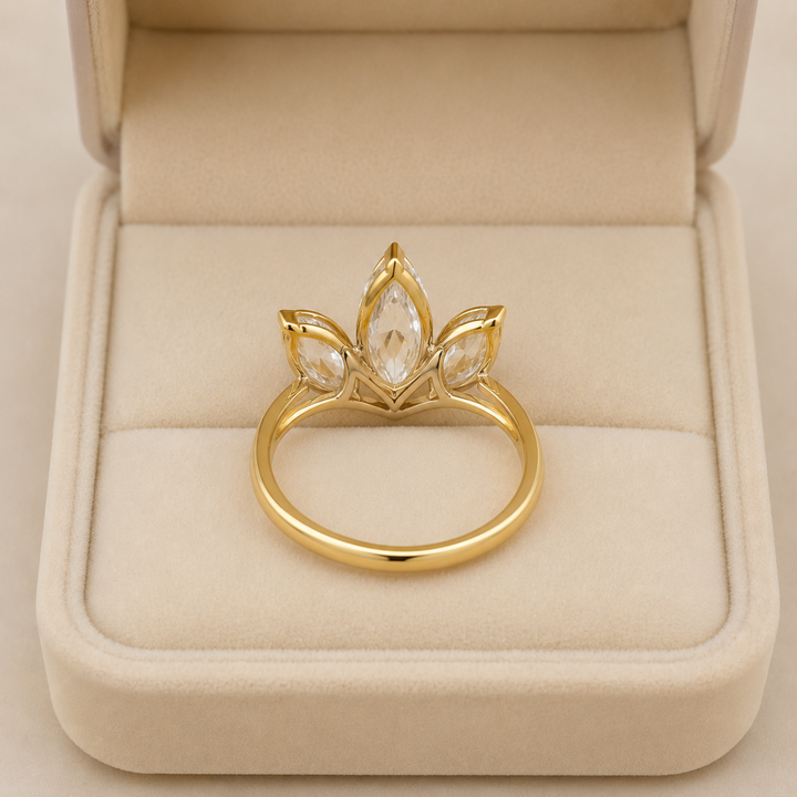 A gold ring with a lotus flower design and clear marquise-cut gemstones, displayed inside an open beige velvet jewelry box.