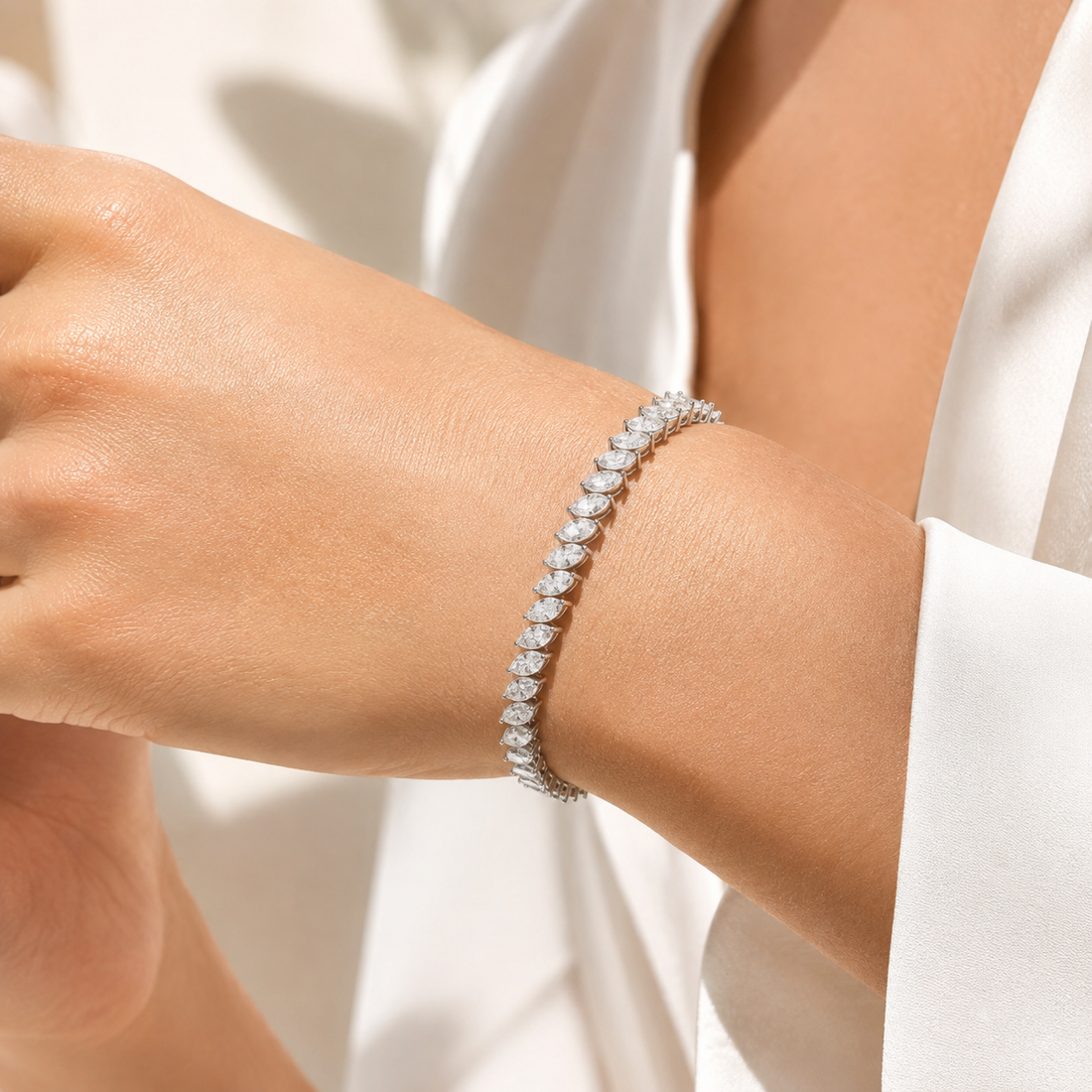 A close-up of a diamond tennis bracelet on a woman's wrist, styled with a white satin blouse.