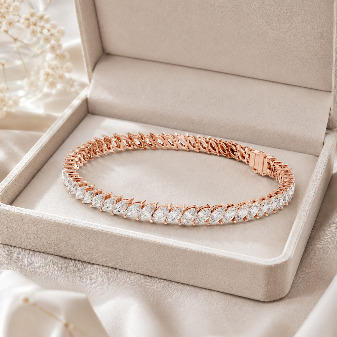 A rose gold tennis bracelet with clear stones, displayed inside an open beige jewelry box on a soft satin fabric background.