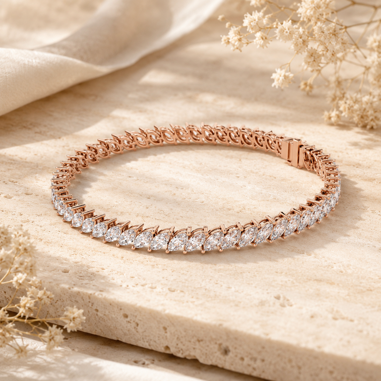 A rose gold tennis bracelet with a row of clear pavé-set stones, displayed on a textured beige stone slab with dried flowers and draped fabric.