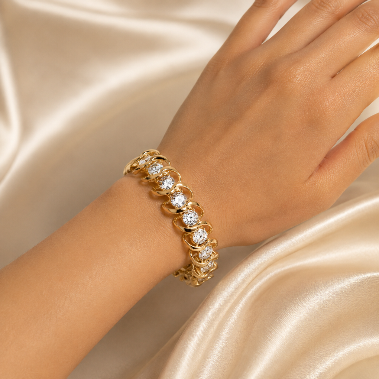 A gold tennis-style bracelet with round clear stones worn on a person's wrist, photographed against draped satin fabric.