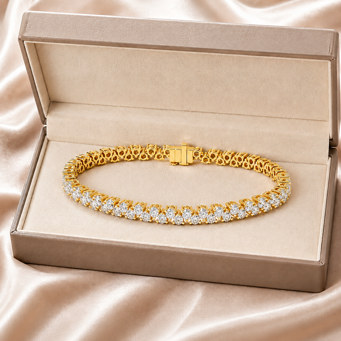 A gold tennis bracelet with clear gemstones, presented inside an open beige jewelry box on a satin fabric background.