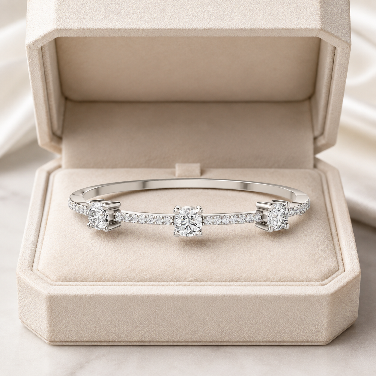 A silver three-stone diamond bangle bracelet displayed inside an open beige velvet jewelry box.