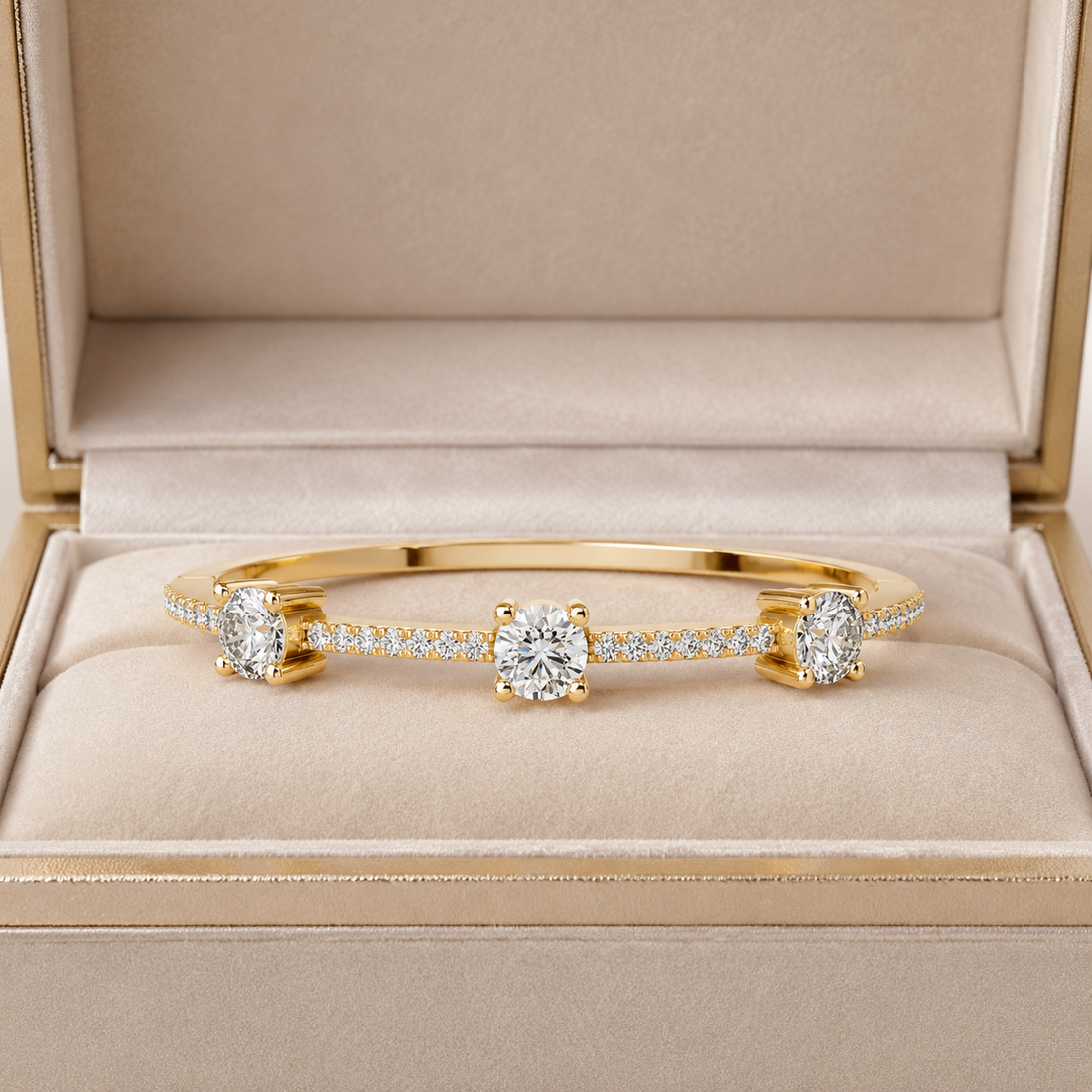 A yellow gold bangle bracelet with three round-cut diamond centers and pavé diamond sections, displayed inside an open beige jewelry box.