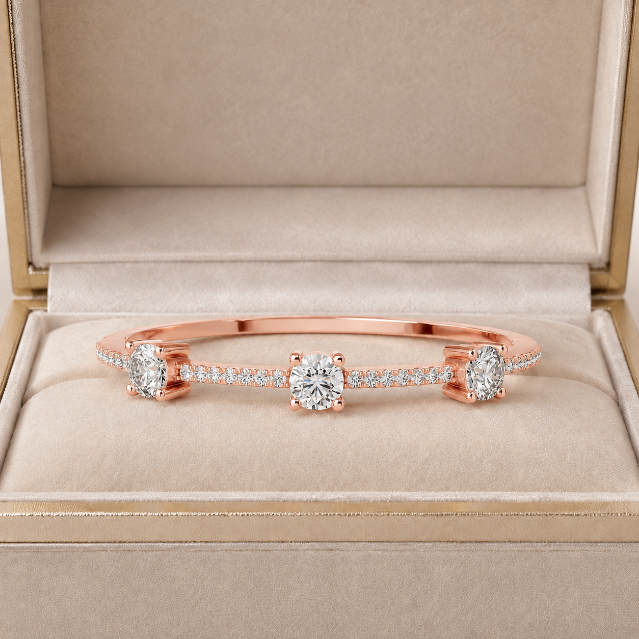A rose gold bangle bracelet with three round-cut center stones and pavé-set side stones, displayed inside an open beige jewelry box.