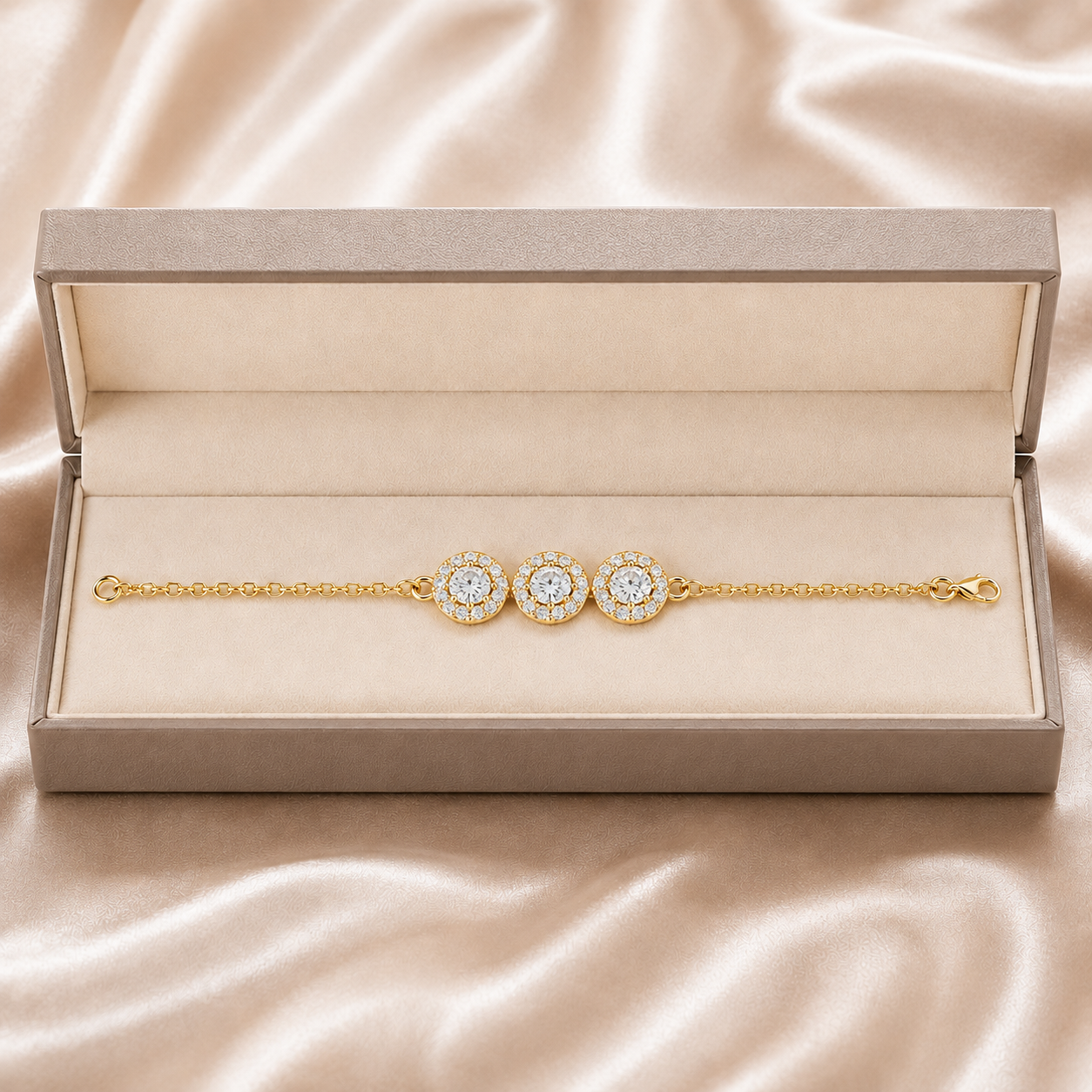 A gold chain bracelet with three round diamond halo centers, presented inside an open beige jewelry box on a champagne satin background.
