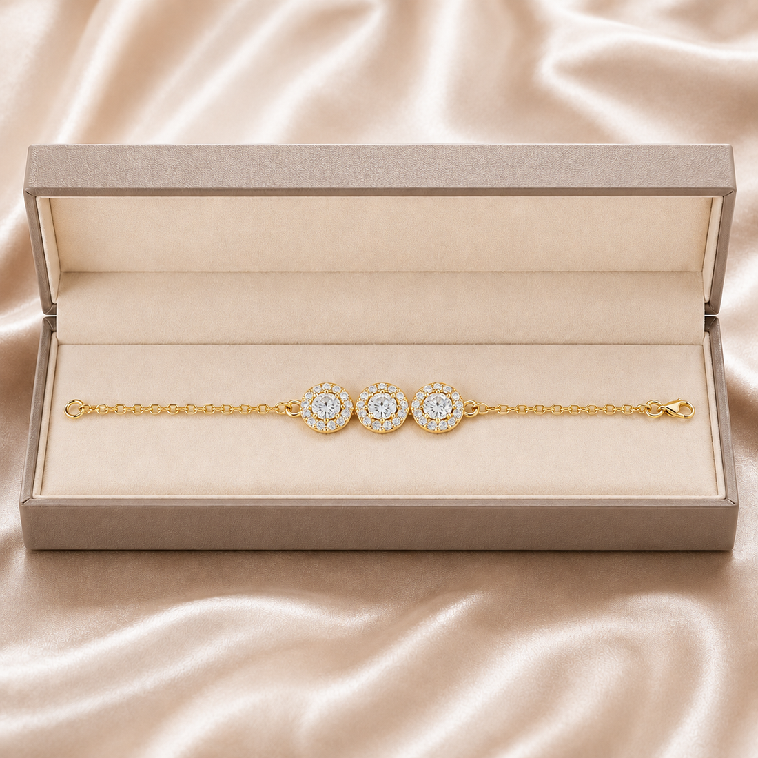 A gold chain bracelet with three round diamond halo centers, presented inside an open beige jewelry box on a champagne satin background.