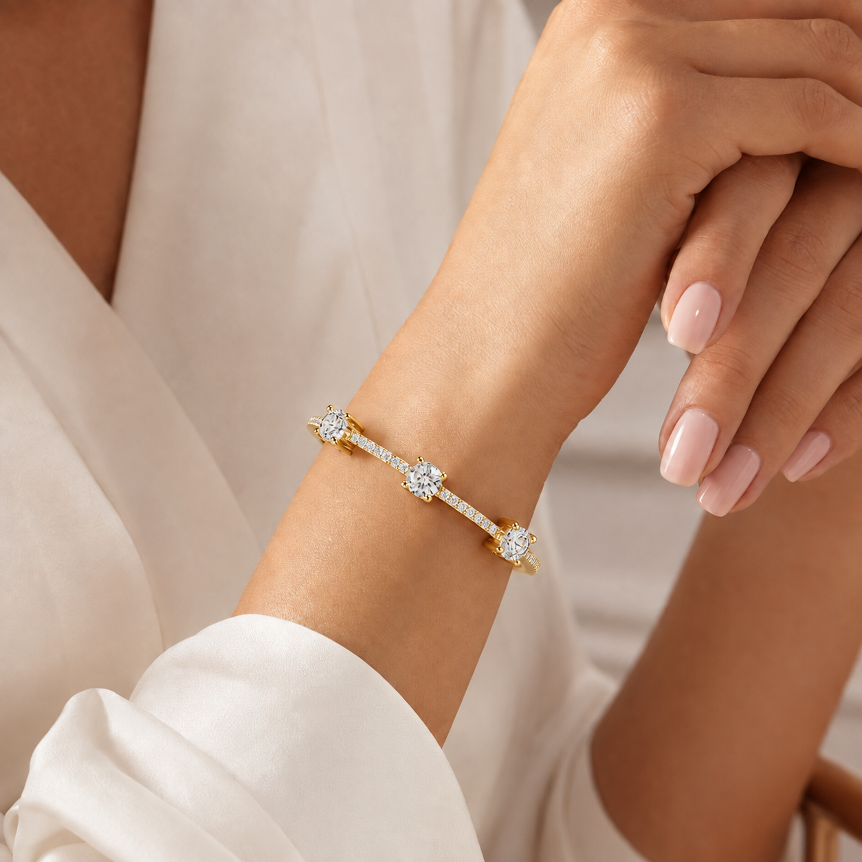 A delicate gold bracelet with three star-shaped diamond clusters, worn on a woman's wrist. The image features a close-up of the hand and wrist, with the person wearing a white satin blouse.