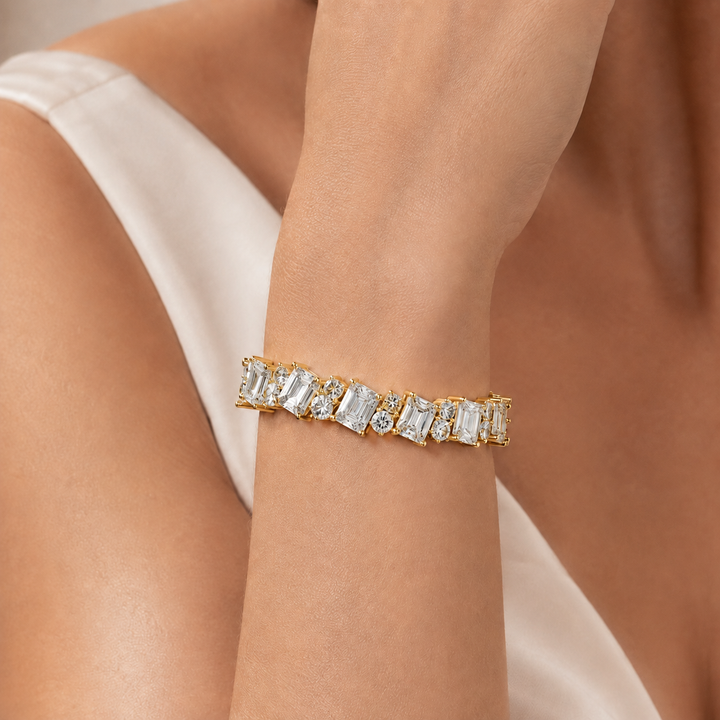 A close-up of a gold bracelet with baguette and round clear stones worn on a woman's wrist, with a white satin top visible in the background.