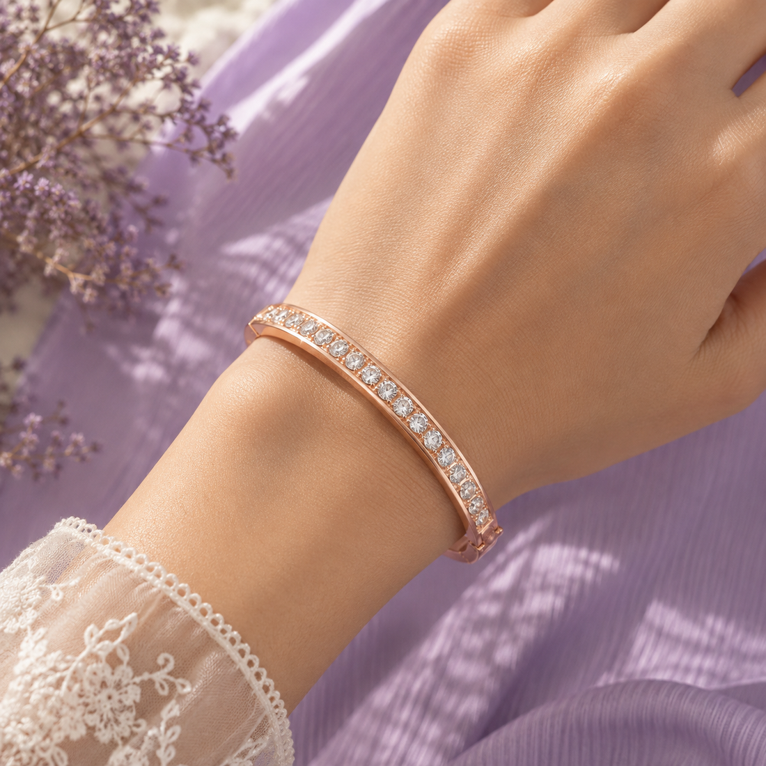 A close-up of a person's wrist wearing a slim rose gold bangle bracelet set with clear pavé stones, styled with a lavender dress and dried lavender flowers.