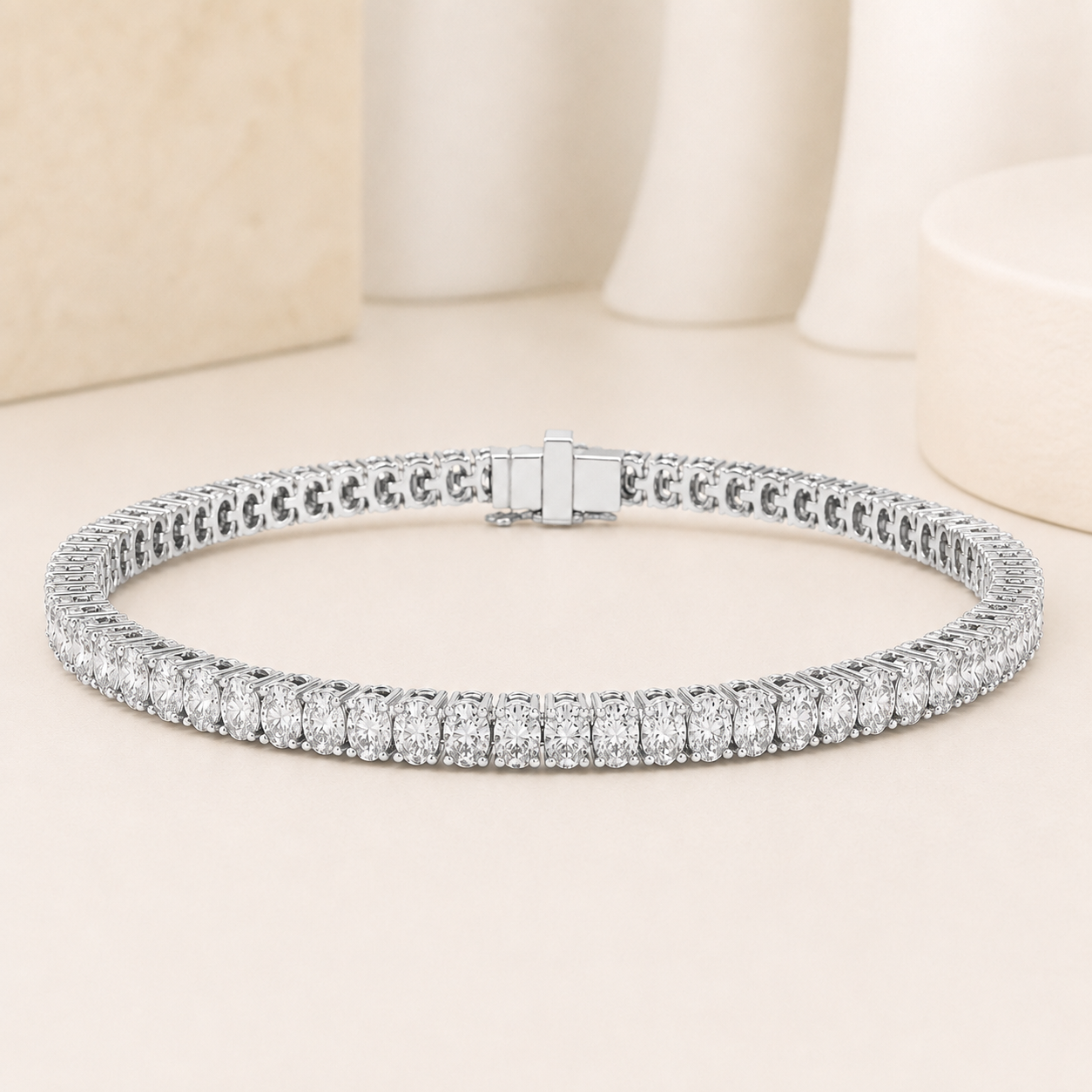 A silver tennis bracelet with a double row of round-cut clear stones, displayed on a light beige surface with soft, blurred decorative background elements.