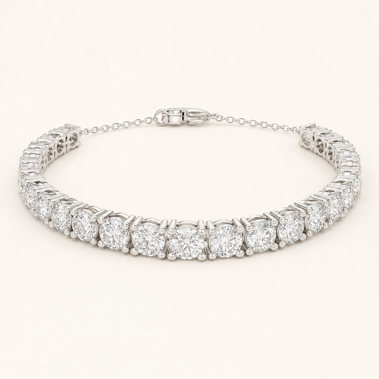 A diamond tennis bracelet in a silver-toned setting, featuring round-cut diamonds in a linked design with a delicate chain extender and clasp, shown on a light cream background.
