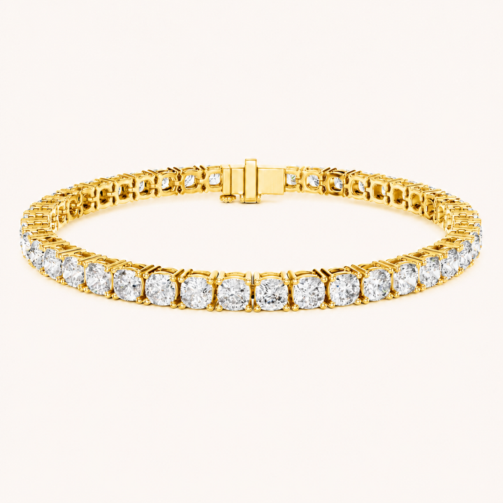A yellow gold tennis bracelet featuring a continuous row of round-cut clear gemstones in a prong setting, shown against a plain off-white background.