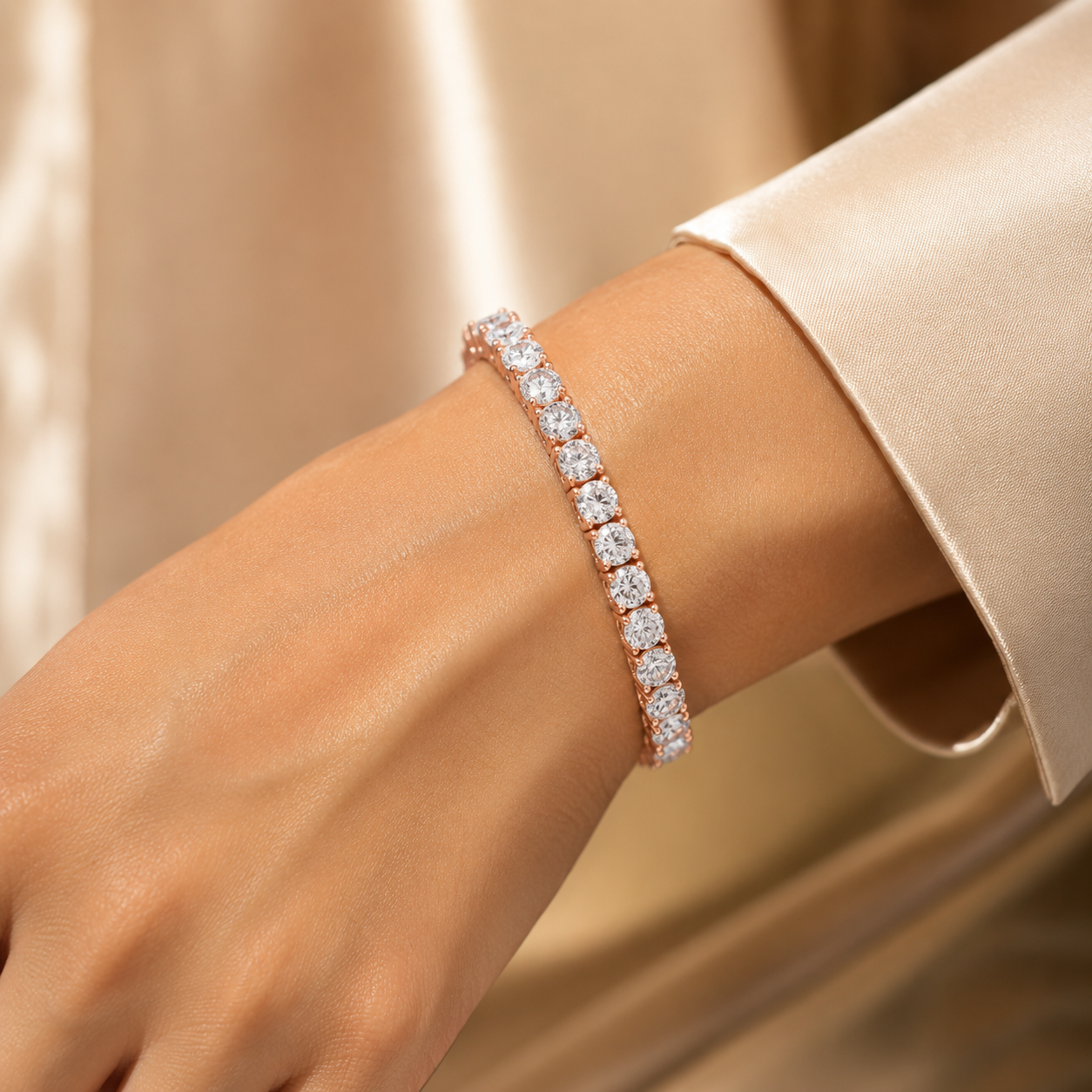 A close-up of a rose gold tennis bracelet with clear square-cut stones worn on a woman's wrist, set against a soft champagne-colored satin background.