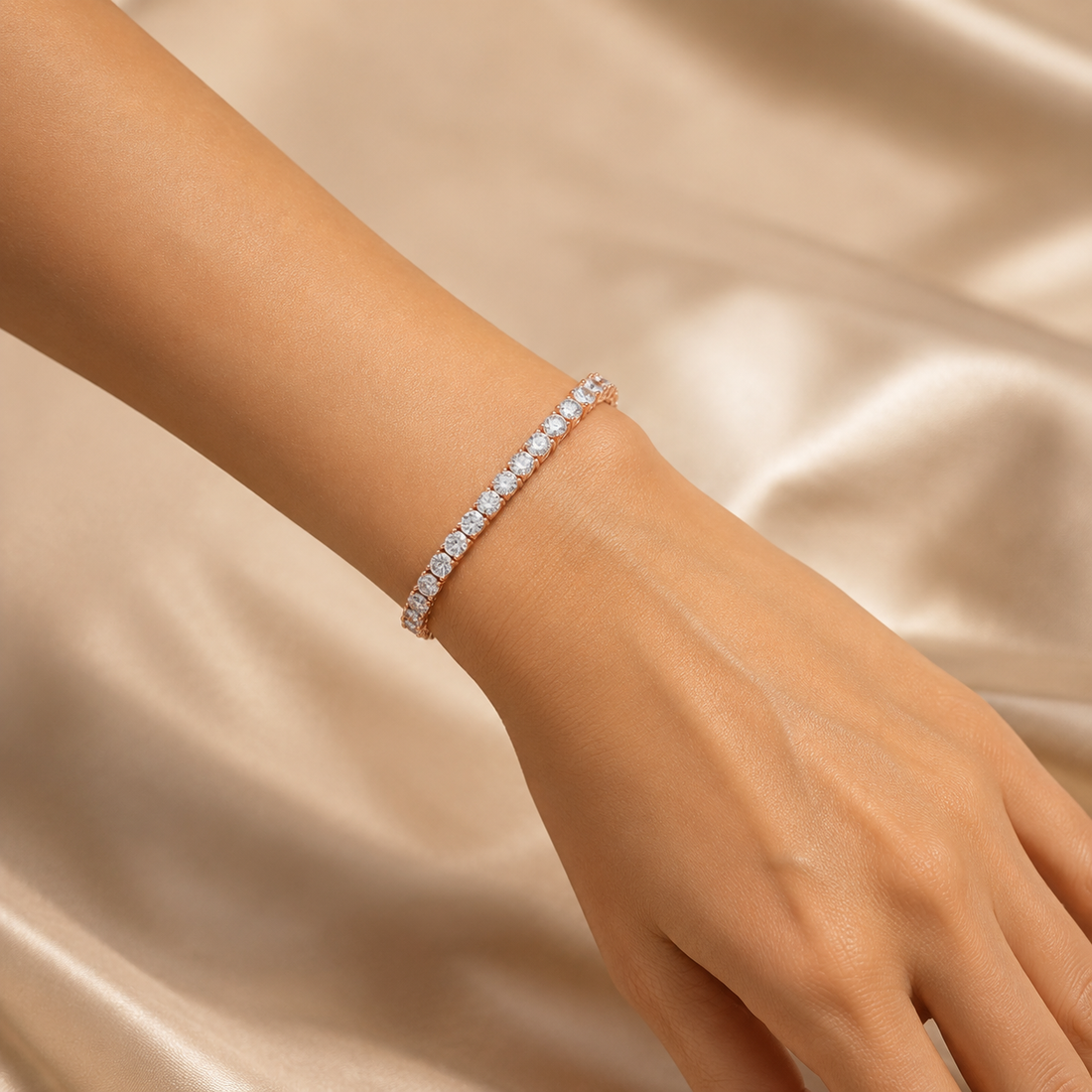 A close-up of a delicate tennis bracelet with clear round-cut stones set in a silver-toned metal, worn on a woman's wrist against a soft beige satin fabric background.