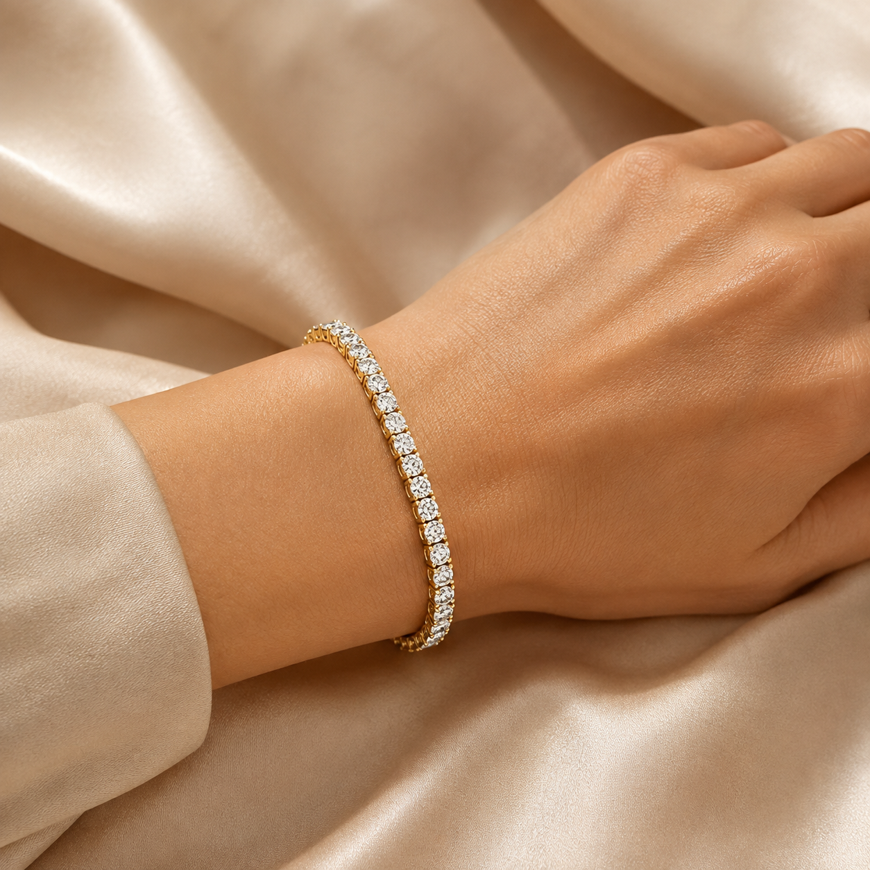 A close-up of a gold tennis bracelet with clear stones worn on a woman's wrist, set against a background of draped champagne-colored satin fabric.