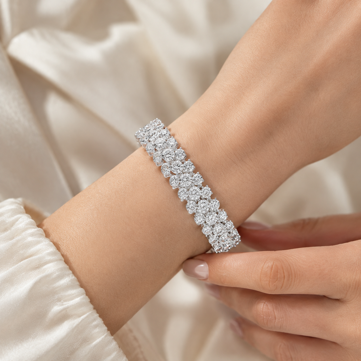 A close-up of a model's wrist wearing a sparkling diamond band bracelet in a silver-toned setting, with elegant cream-colored satin fabric in the background.