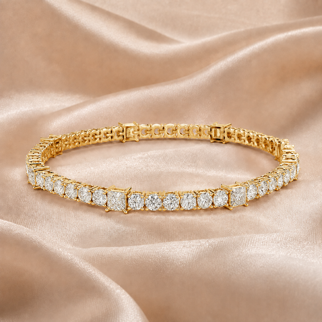 A yellow gold tennis bracelet with square-cut diamonds, displayed on a draped champagne satin fabric background.