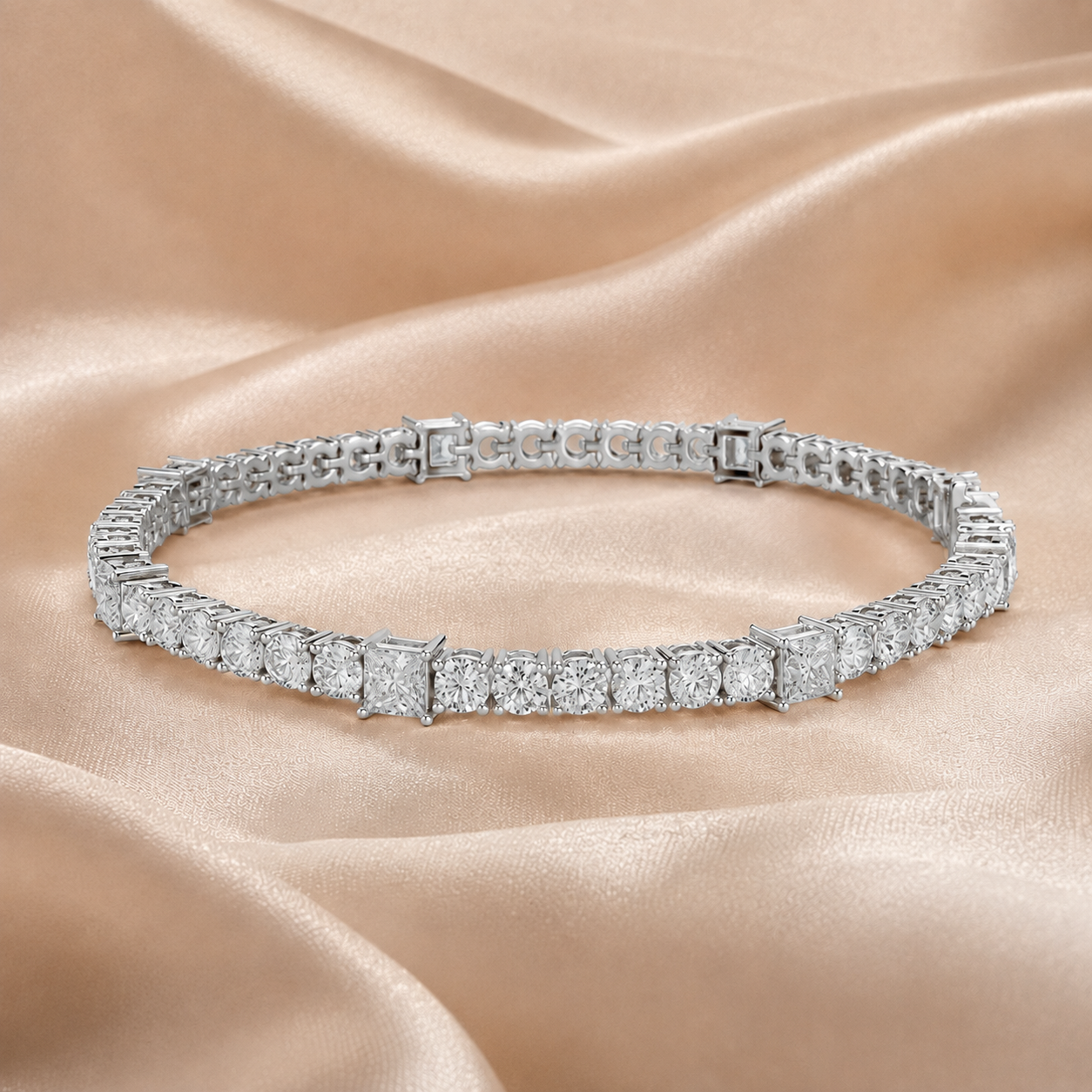 A silver tennis bracelet set with square-cut diamonds, displayed on a draped champagne-colored satin fabric.