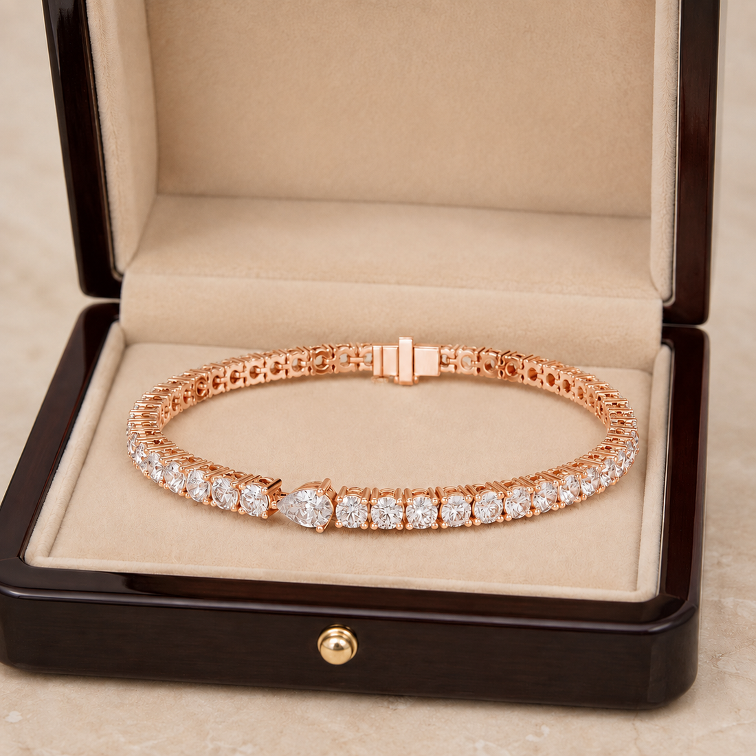 A rose gold tennis bracelet with clear gemstones, displayed inside an open dark wood jewelry box with a beige velvet lining.