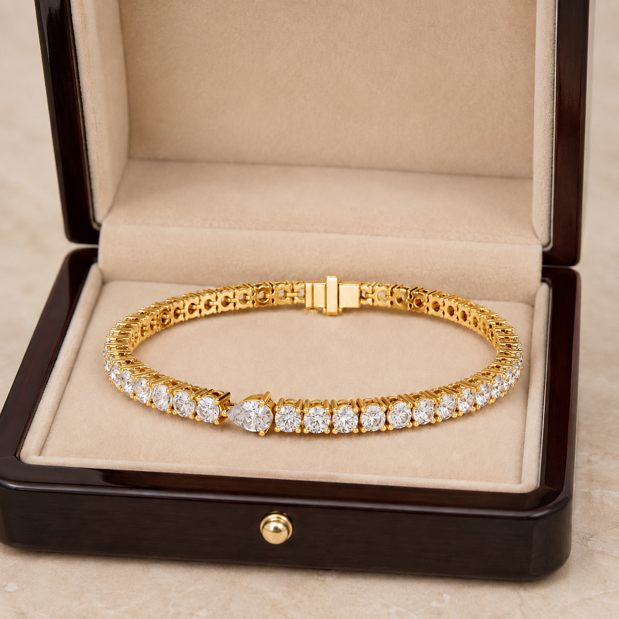 A gold tennis bracelet with a row of clear stones, displayed inside an open dark wood jewelry box with a beige velvet lining.