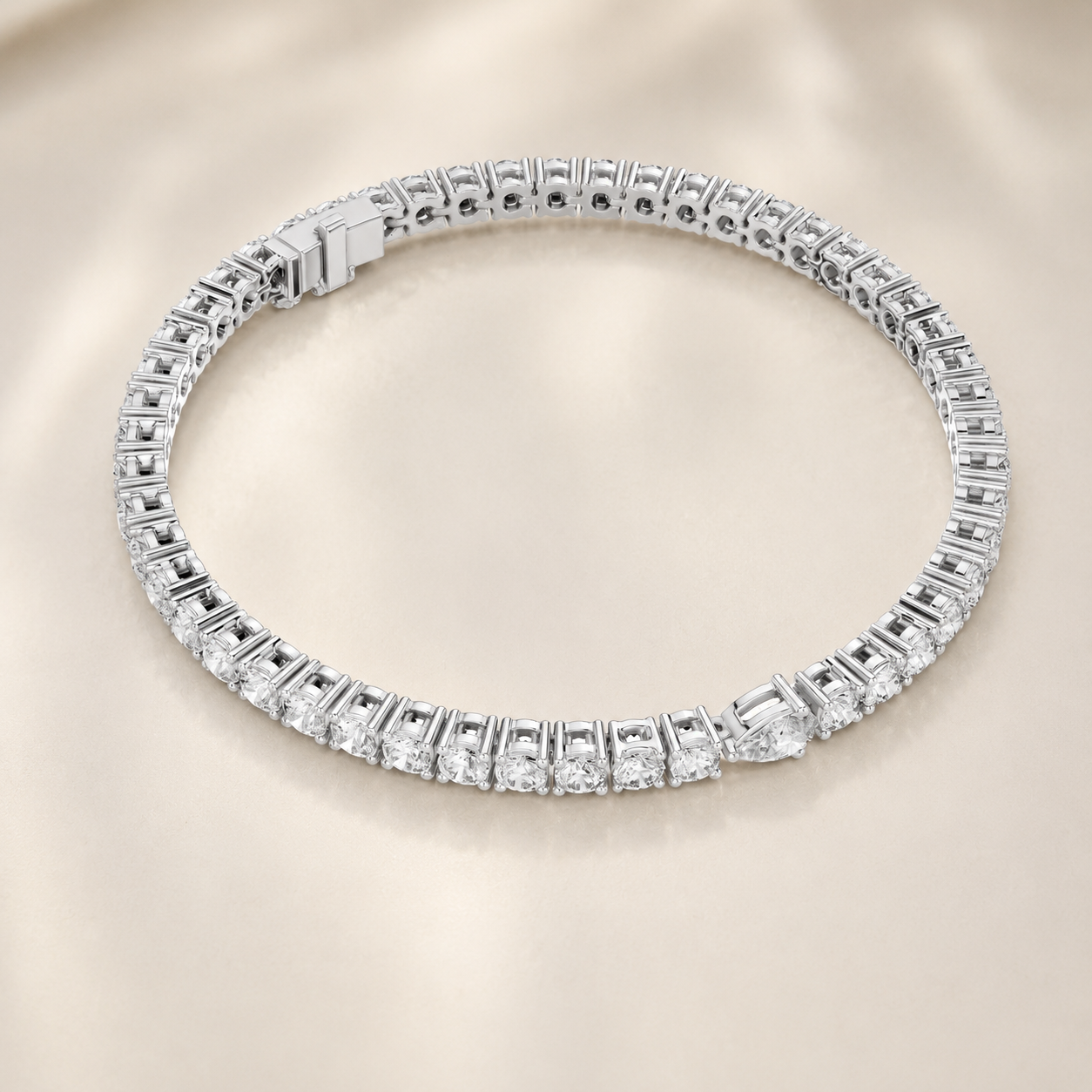 A silver tennis bracelet paved with sparkling clear gemstones, displayed on a soft beige satin background.