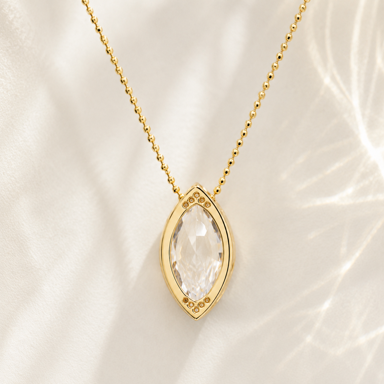 Gold necklace with a marquise-cut clear gemstone pendant, displayed on a soft white fabric background with delicate shadows.