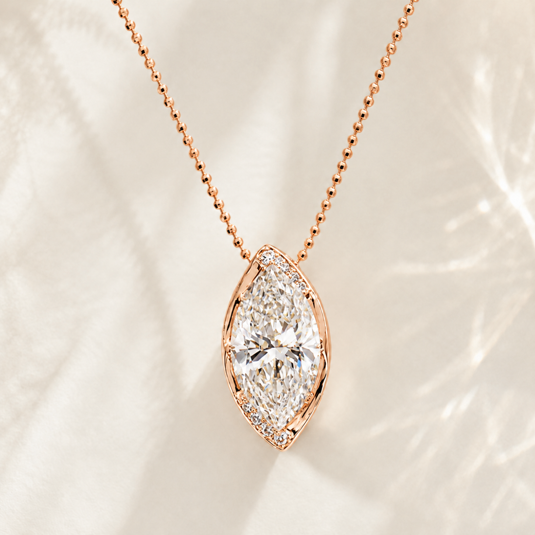 Rose gold necklace with a marquise-shaped diamond pendant, displayed on a soft, light-colored textured fabric background.