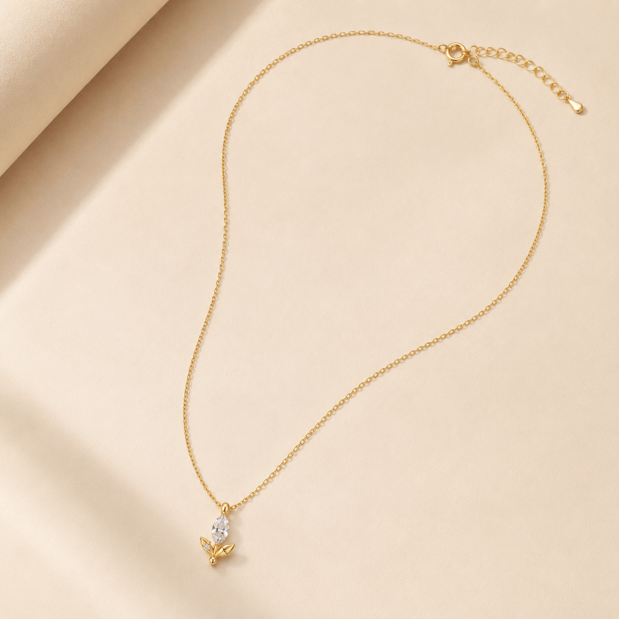 A delicate gold chain necklace with a small butterfly pendant featuring a clear teardrop gemstone, displayed on a soft beige fabric background.