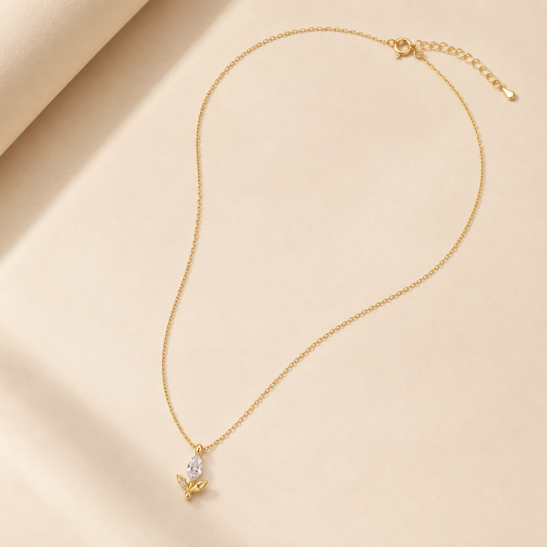 A delicate gold chain necklace with a small butterfly pendant featuring a clear teardrop gemstone, displayed on a soft beige fabric background.