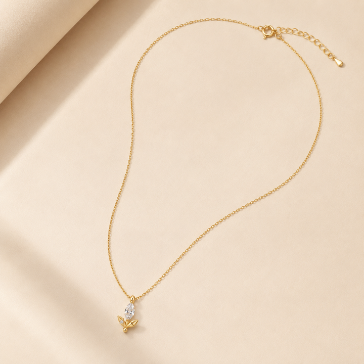 A delicate gold chain necklace with a small butterfly pendant featuring a clear teardrop gemstone, displayed on a soft beige fabric background.