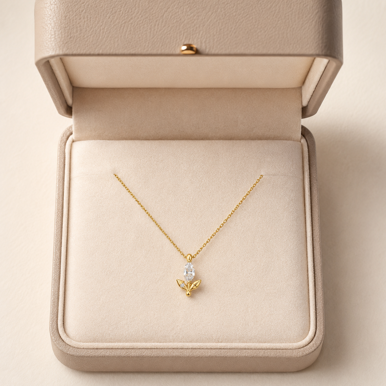 A delicate gold necklace with a small bow and clear teardrop gemstone pendant, displayed inside an open beige jewelry box.