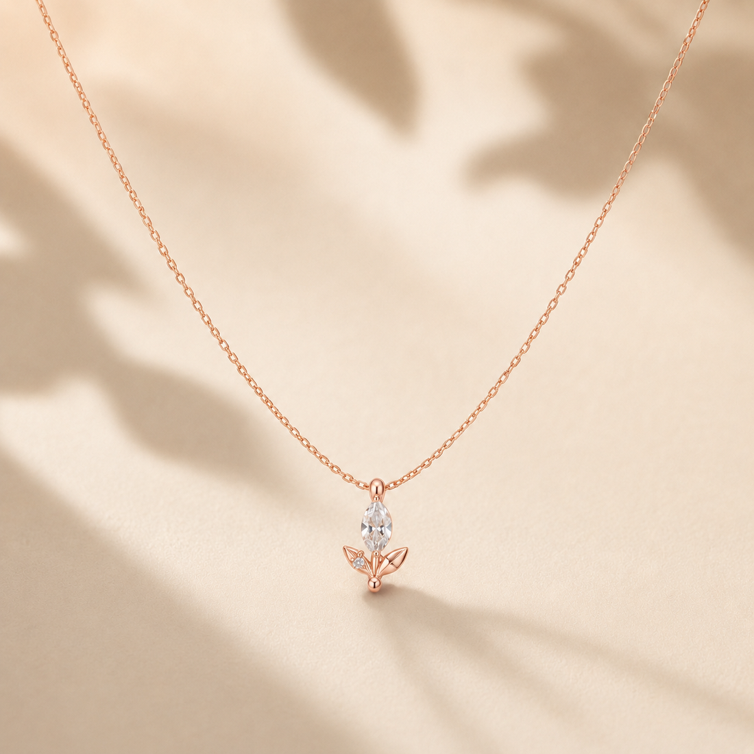 A delicate rose gold chain necklace with a small butterfly pendant featuring a marquise-cut clear gemstone, displayed on a warm beige background with soft leaf shadows.